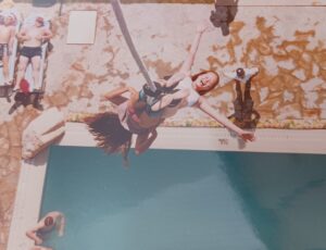 A picture of a tandem bungee jump. Toni is attached to her friend. Toni is looking up at the camera with her arms outstretched and is smiling