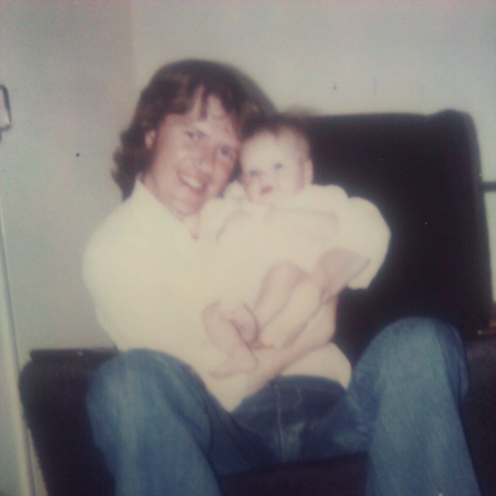 Social mobility and resilience - a picture of Toni's dad holding her when she was around 6 months old. he is sat in a chair and wearing blue denim flared jeans and a white shirt