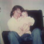 Social mobility and resilience - a picture of Toni's dad holding her when she was around 6 months old. he is sat in a chair and wearing blue denim flared jeans and a white shirt