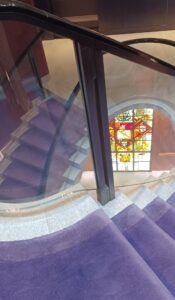 a grand spiral staircase with thick lilac carpeting