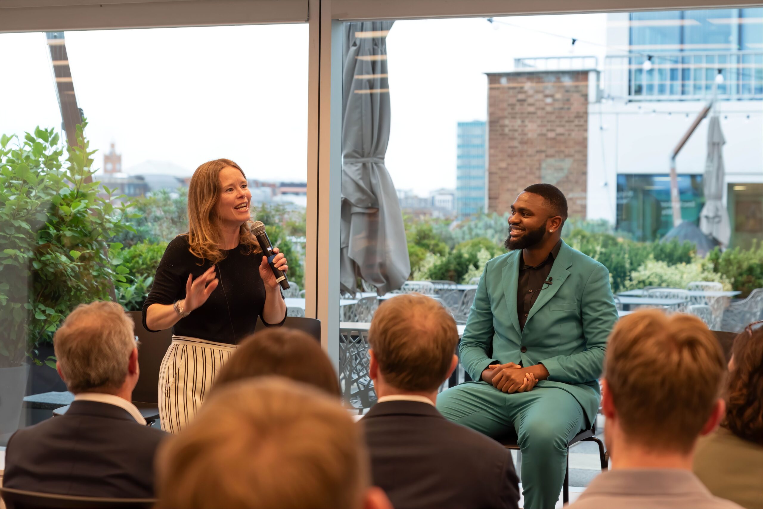 Toni Kent is talking about Social Mobility, she is stood, holding a mic in her left hand. She is being watched by Austin Okolo who is there to talk about Generation Z