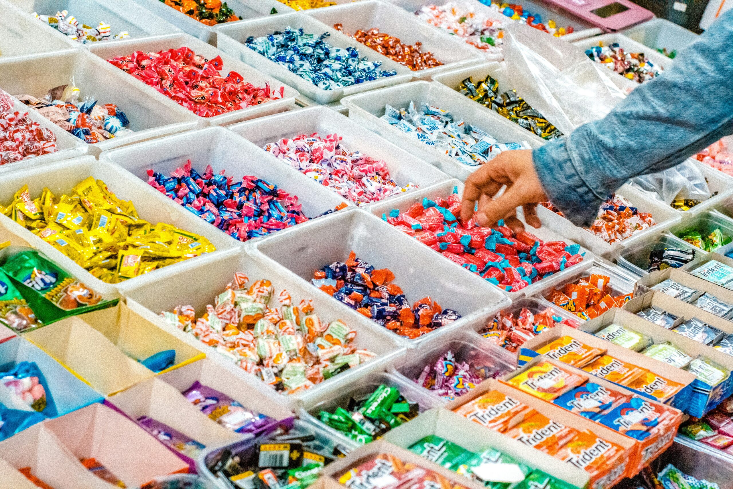 a picture of a pick and mix - lots of sweets in open boxes with a hand reaching in to take a sweet!