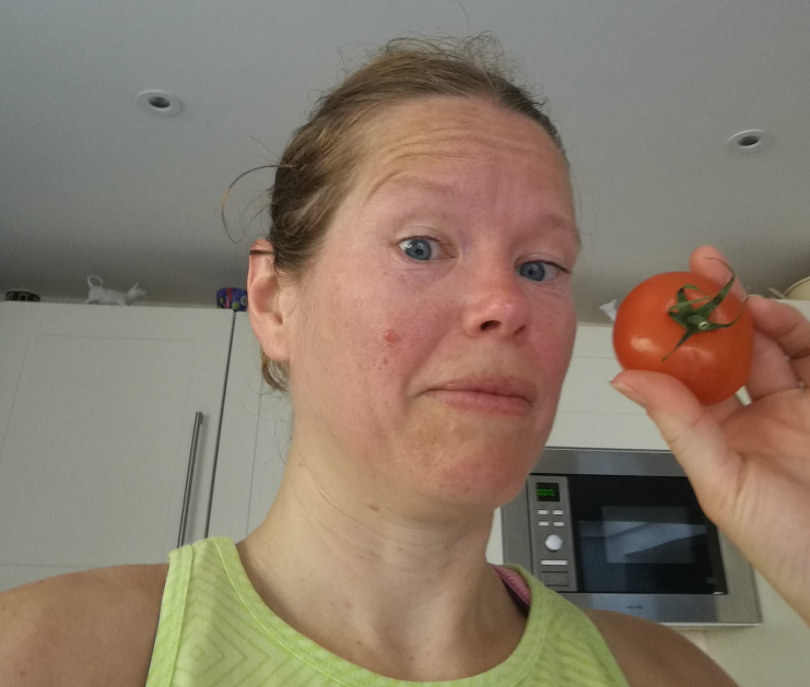 a picture of Toni after she's been for a run. her hair is tied back and she is holding a tomato next to her bright red face